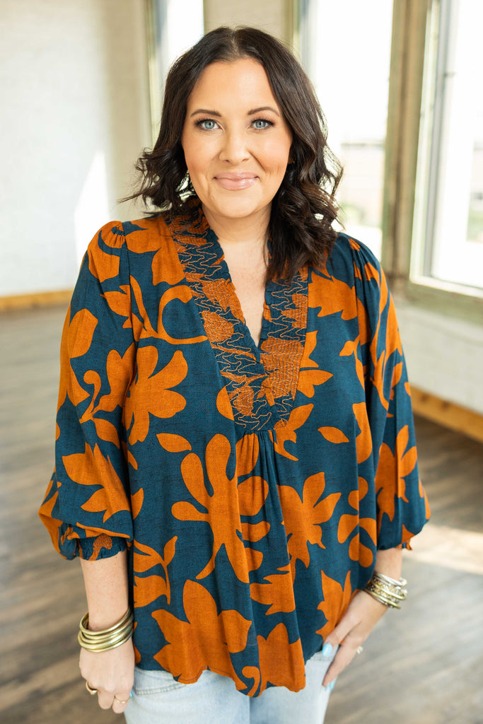 Plus-size woman wearing a flowy teal and burnt orange floral printed challis top with long balloon sleeves and smocked neckline.