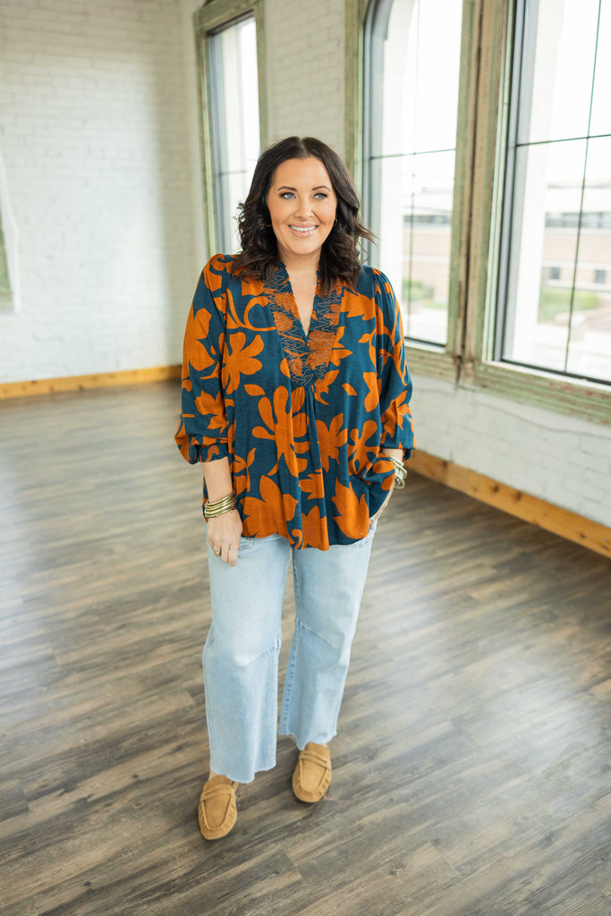 Plus-size woman wearing a flowy teal and burnt orange floral printed challis top with long balloon sleeves and smocked neckline.