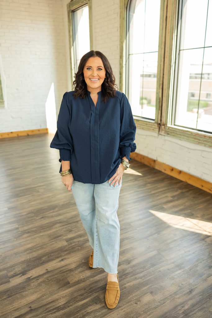 Plus-size woman wearing a navy textured blouse with smocked 3/4 sleeves and a V neckline.