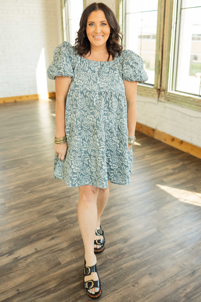 Plus-size woman wearing a blue jacquard floral babydoll mini dress with puff sleeves and a square neckline.