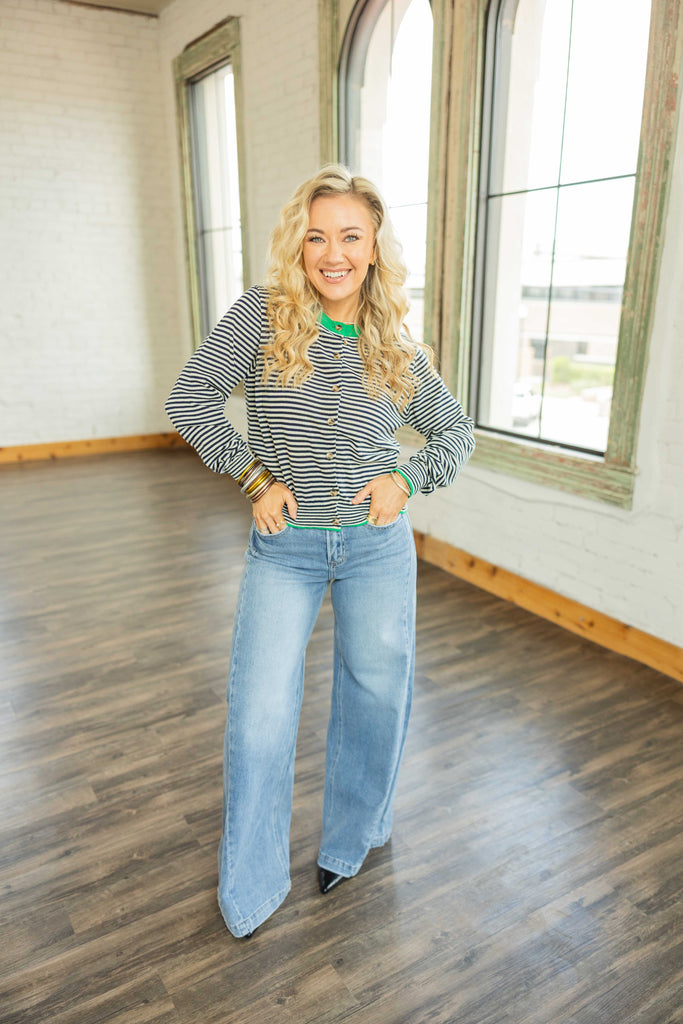 Blonde woman wearing the Vervet Olivia Mid Rise Palazzo Jeans in light wash denim with seam detail and wide leg fit, styled with a cropped button-up top, standing in a bright room with wood floors.
