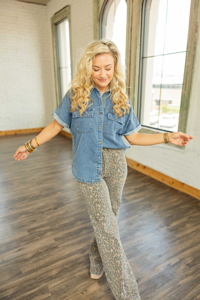 Woman wearing [RISEN] denim rolled cap sleeve button up top with oversized fit and front flap pockets.