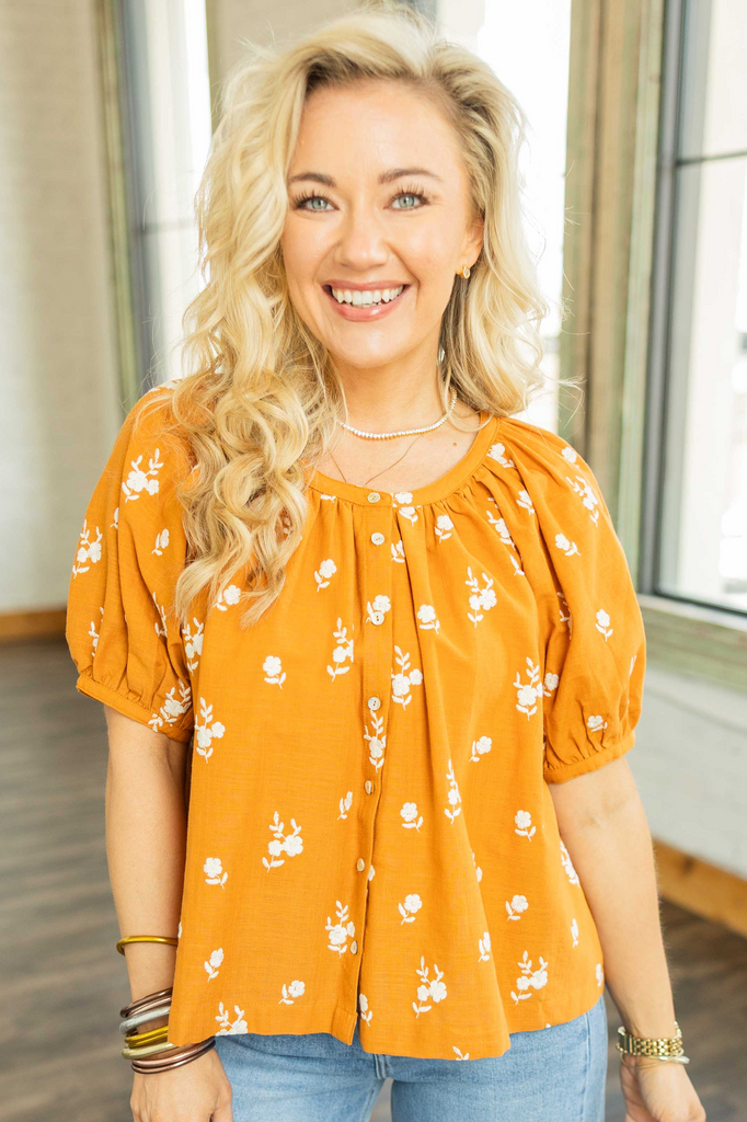  Woman wearing auburn floral embroidered button up cotton blouse with puff sleeves.
