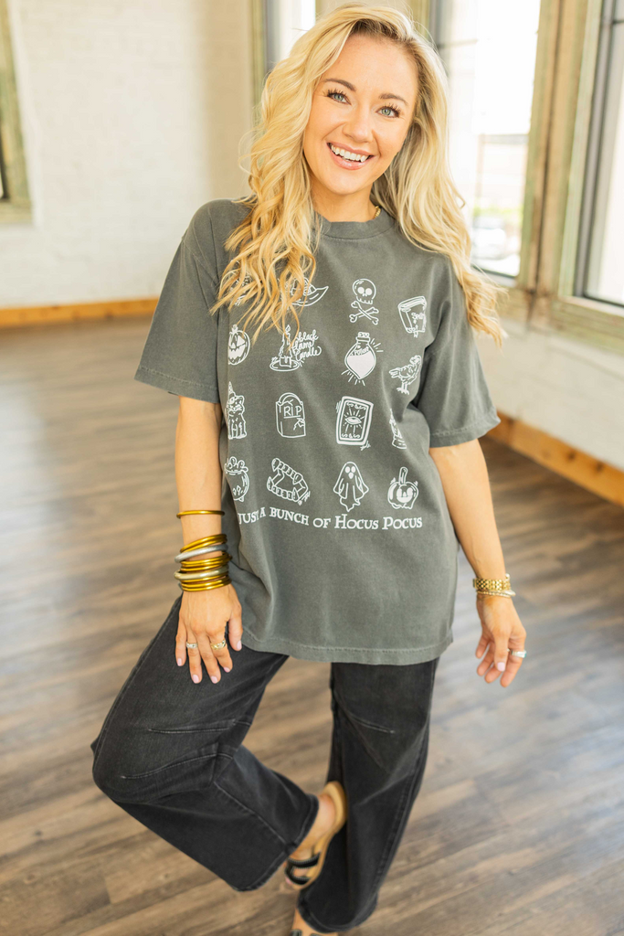 Woman wearing a dark gray graphic tee with white Halloween icons and text reading “It’s Just a Bunch of Hocus Pocus.”