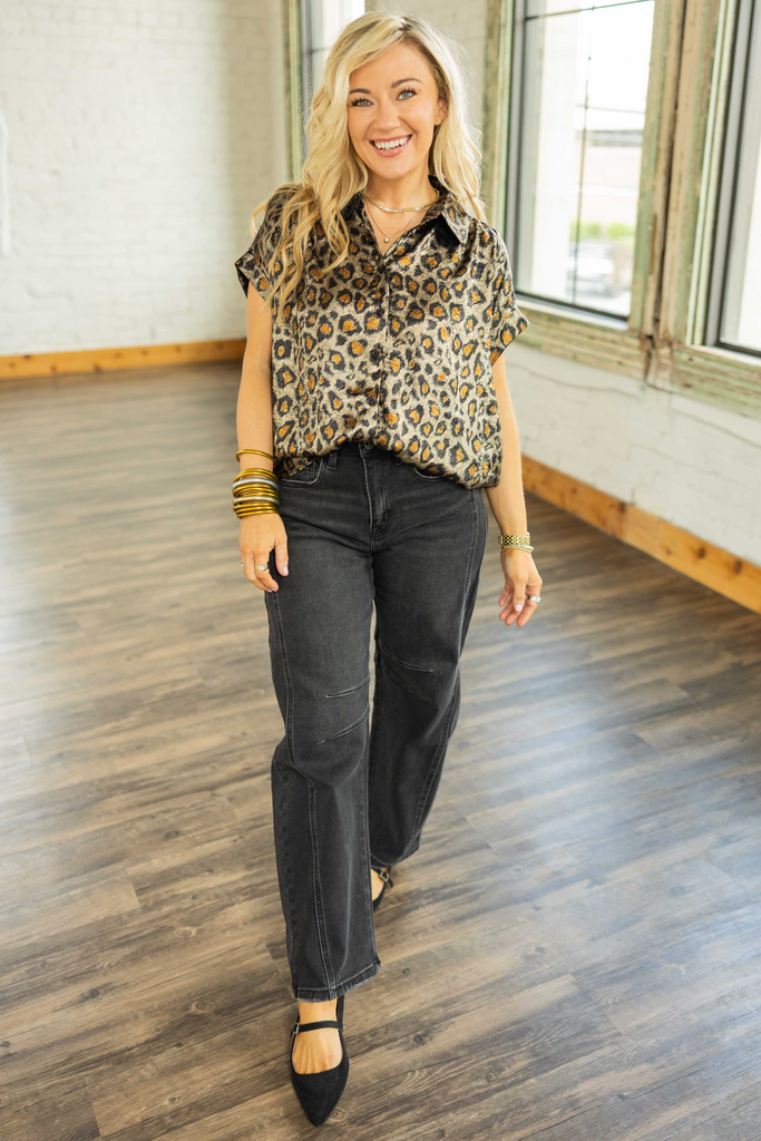 Woman wearing a metallic leopard print button down top with cuffed short sleeves, ruched shoulders, and a flowy high-low hem.