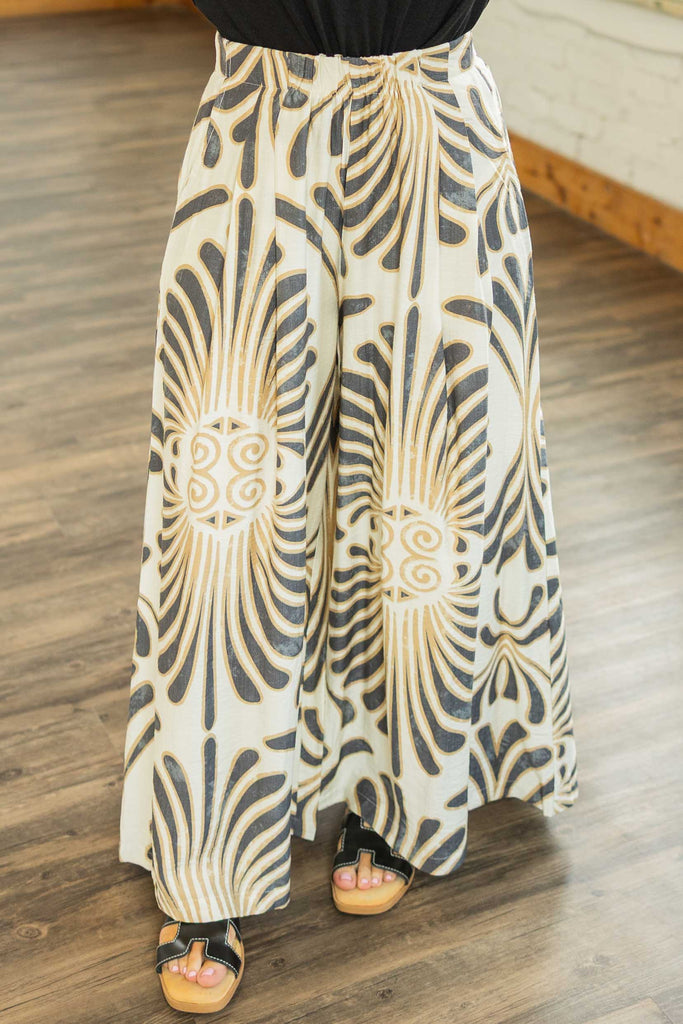 Woman wearing cream wide leg pants with bold black and tan abstract print, styled with a tucked black top.