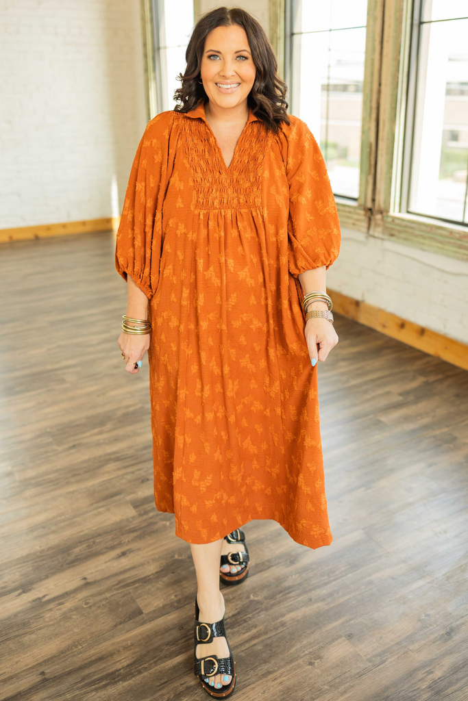 PLUS SIZE Woman wearing a rust textured maxi dress with ruched collar detail and 3/4 sleeves, styled with sandals.