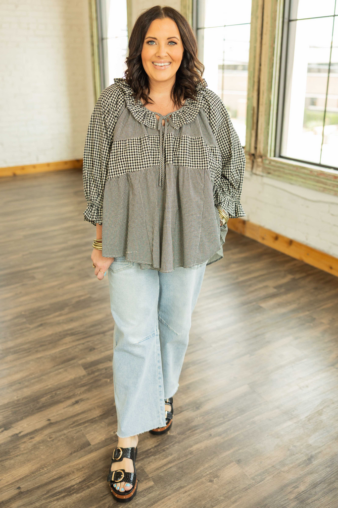 Woman wearing a plus-size black and ivory gingham top with ruffle sleeves, tie-front neckline, and high-low hem.