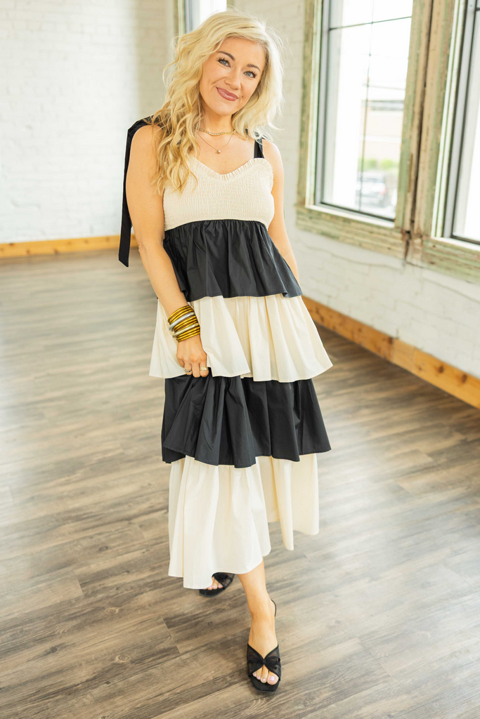 Woman wearing a cream and black colorblock ruffle tiered maxi dress with smocked bodice and tie straps.