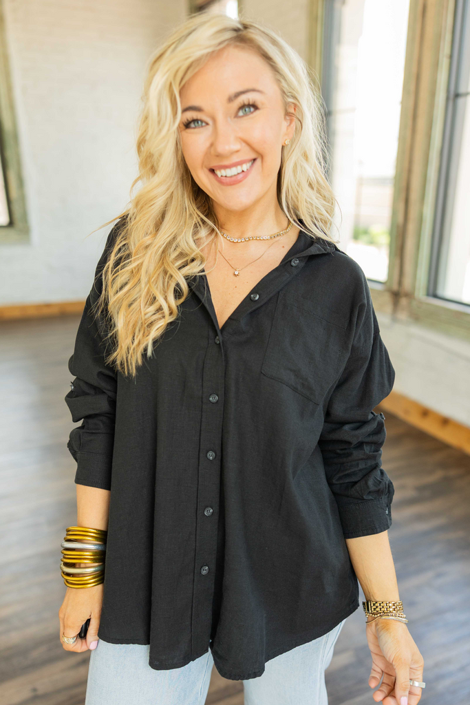 Woman wearing an oversized black linen blend button-up top with roll-tab sleeves and relaxed fit.