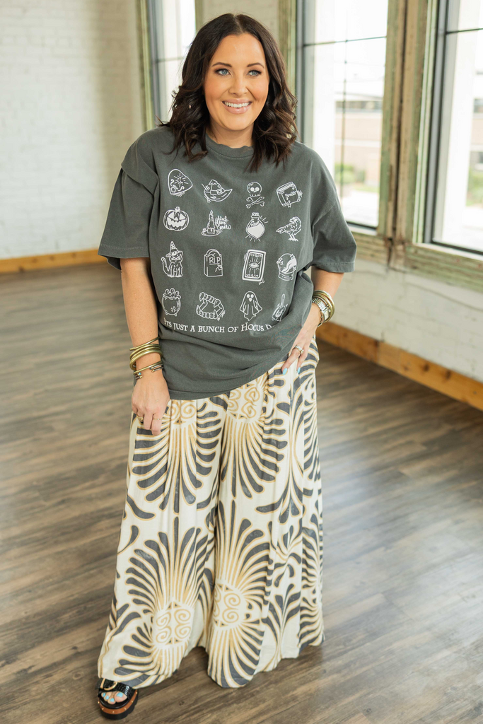 Woman wearing cream wide leg pants with bold black and gold abstract shell print and a relaxed, flowy fit.