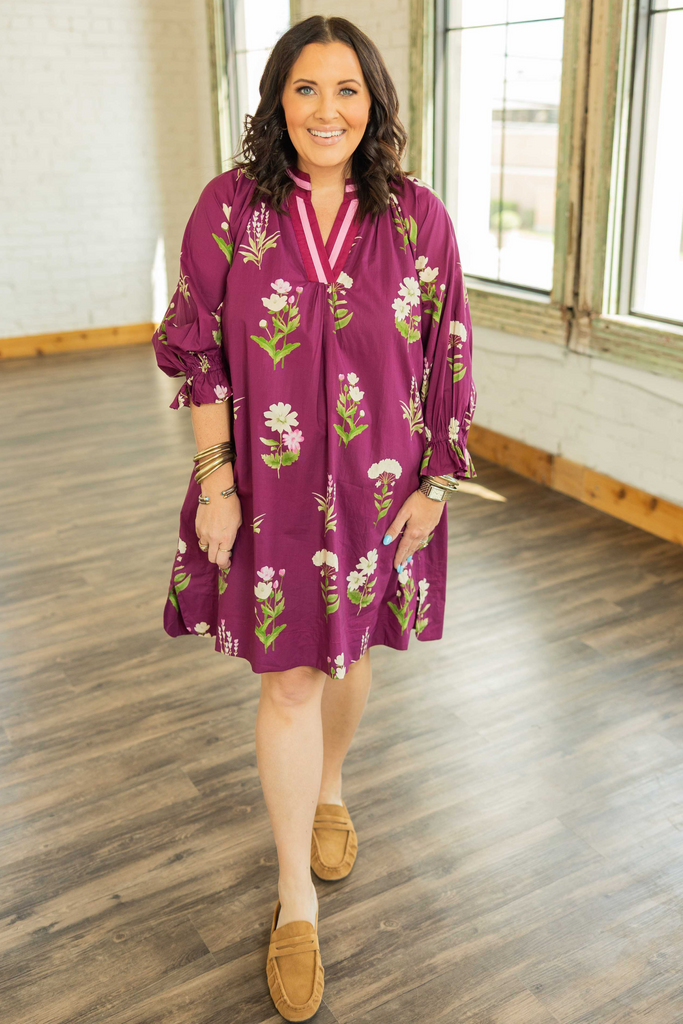 PLUS SIZE CURVY WOMAN wearing a plum floral tunic mini dress with 3/4 ruffle sleeves, contrast V-neckline, and side pockets