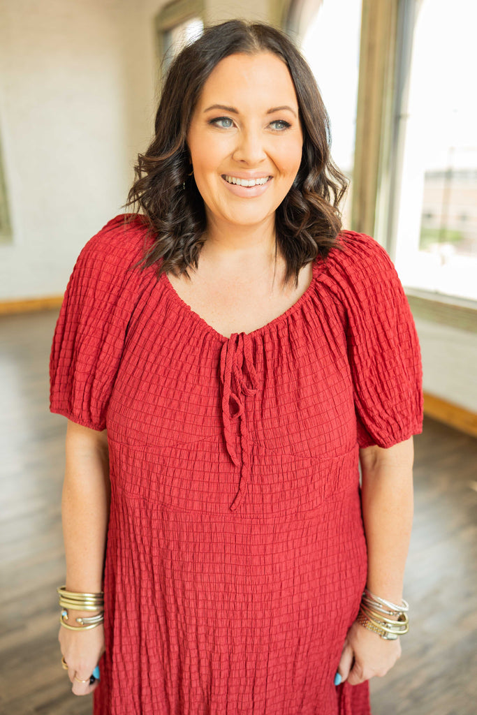 brunette plus sized woman wearing a red smocked boho midi dress with puff sleeves and tiered skirt.