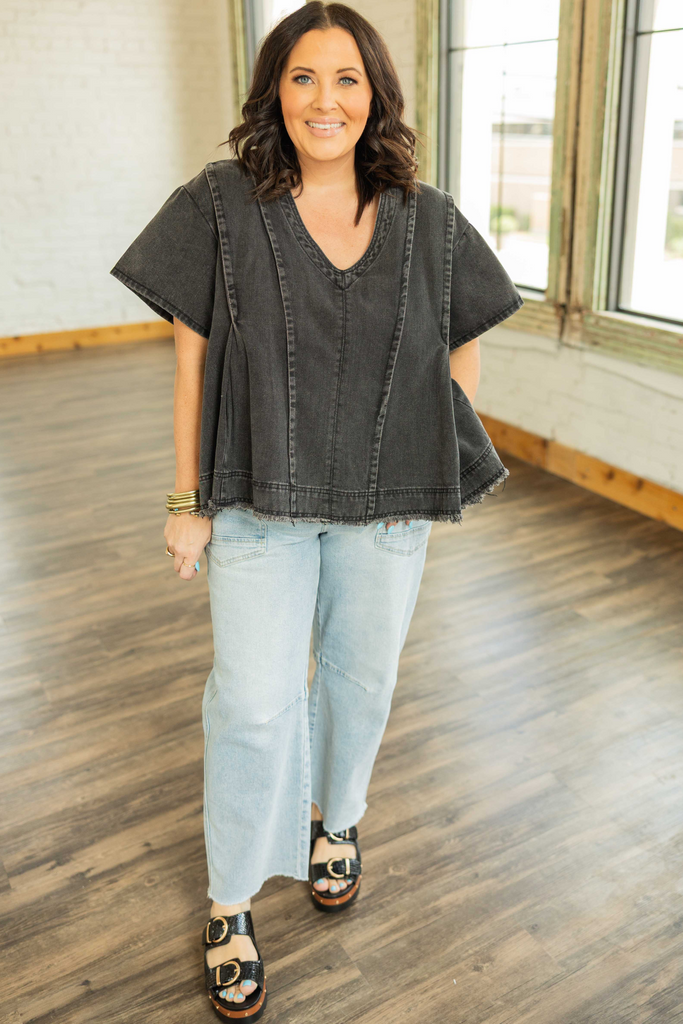 CURVY Woman wearing a washed black denim v-neck top with exposed seams and frayed hem styled with light wash jeans.