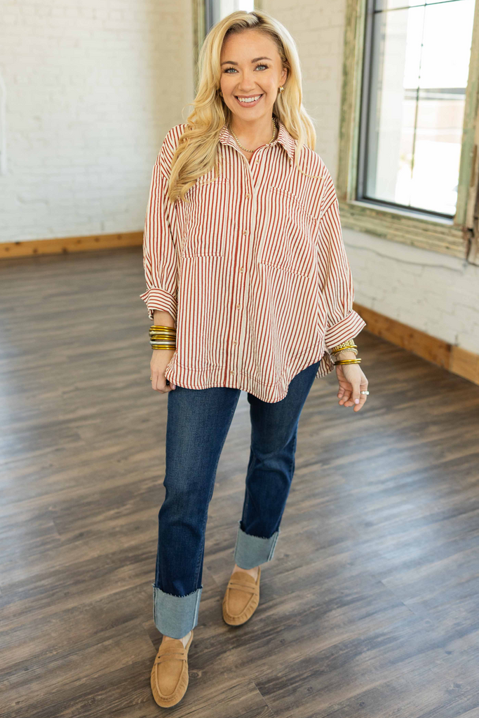 Woman wearing a striped shirt, jeans, and brown shoes indoors.