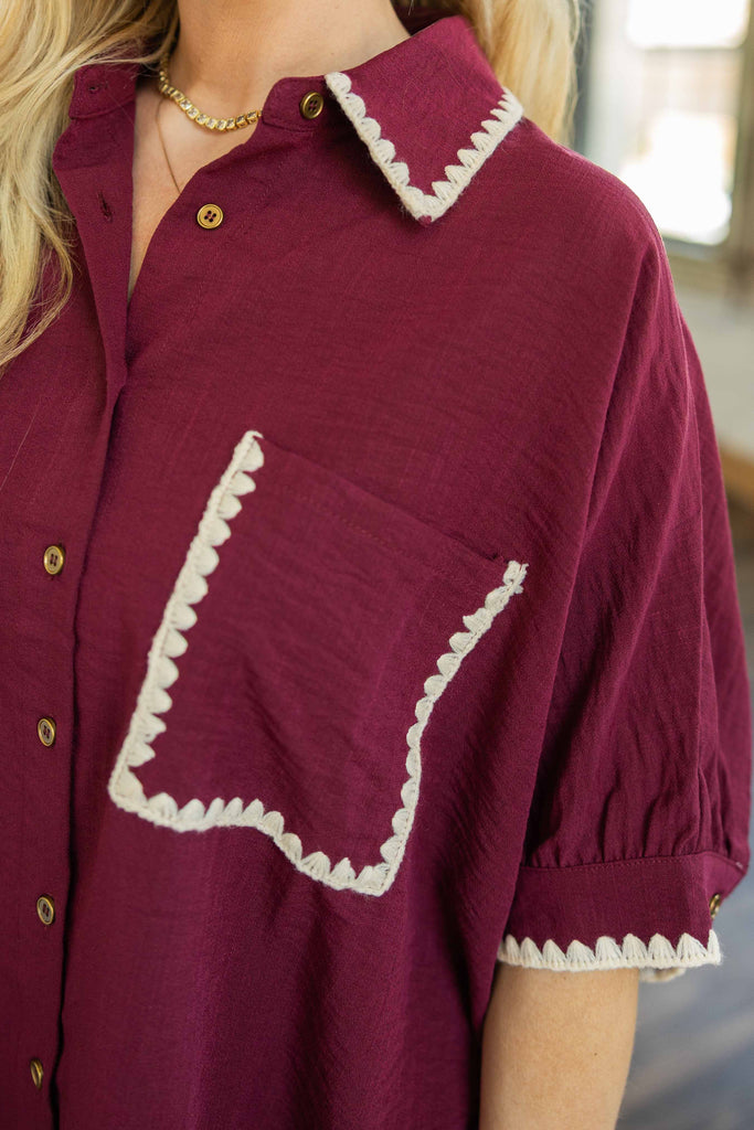 Close-up of a burgundy shirt with white trim on collar and pocket, worn by a person.
