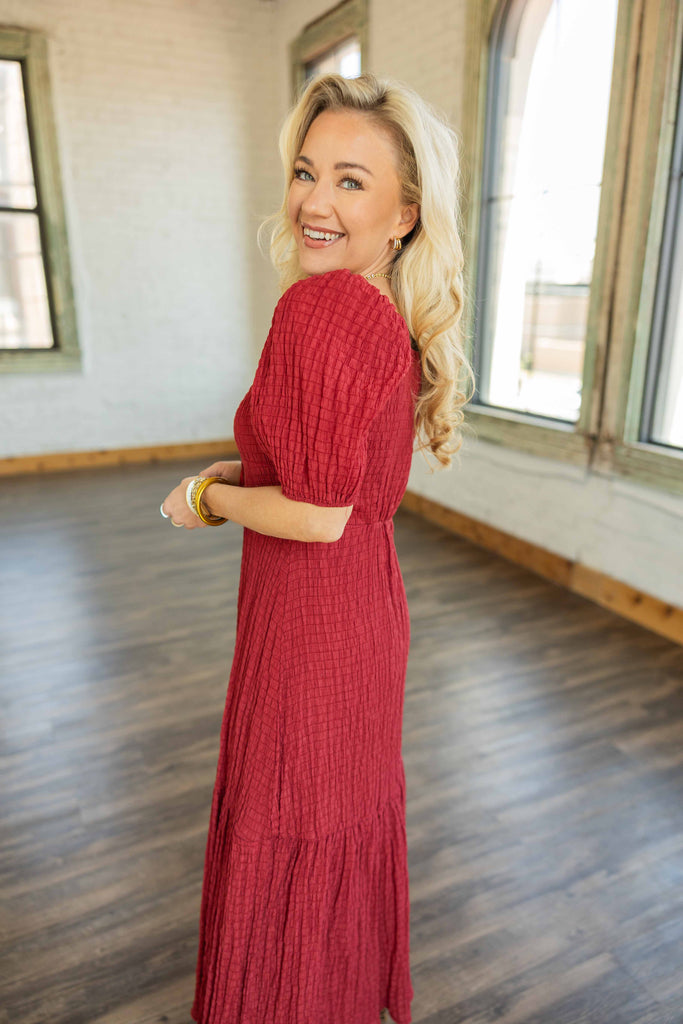 Blonde woman wearing a red smocked boho midi dress with puff sleeves and tiered skirt.