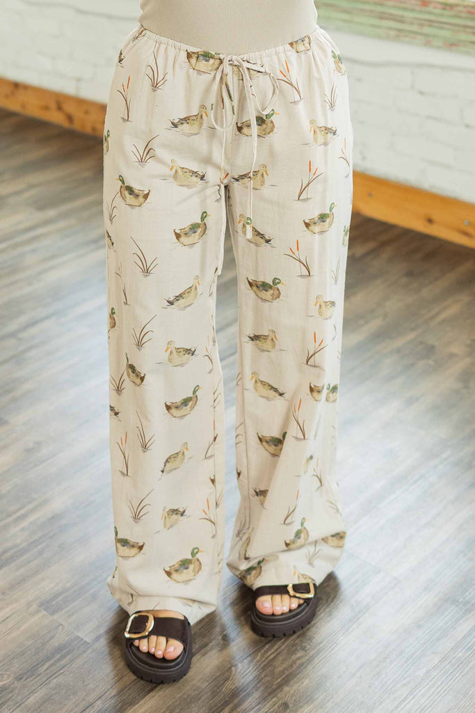 Woman wearing cream wide leg drawstring pants with mallard duck print paired with a red bird graphic sweater in a bright loft.