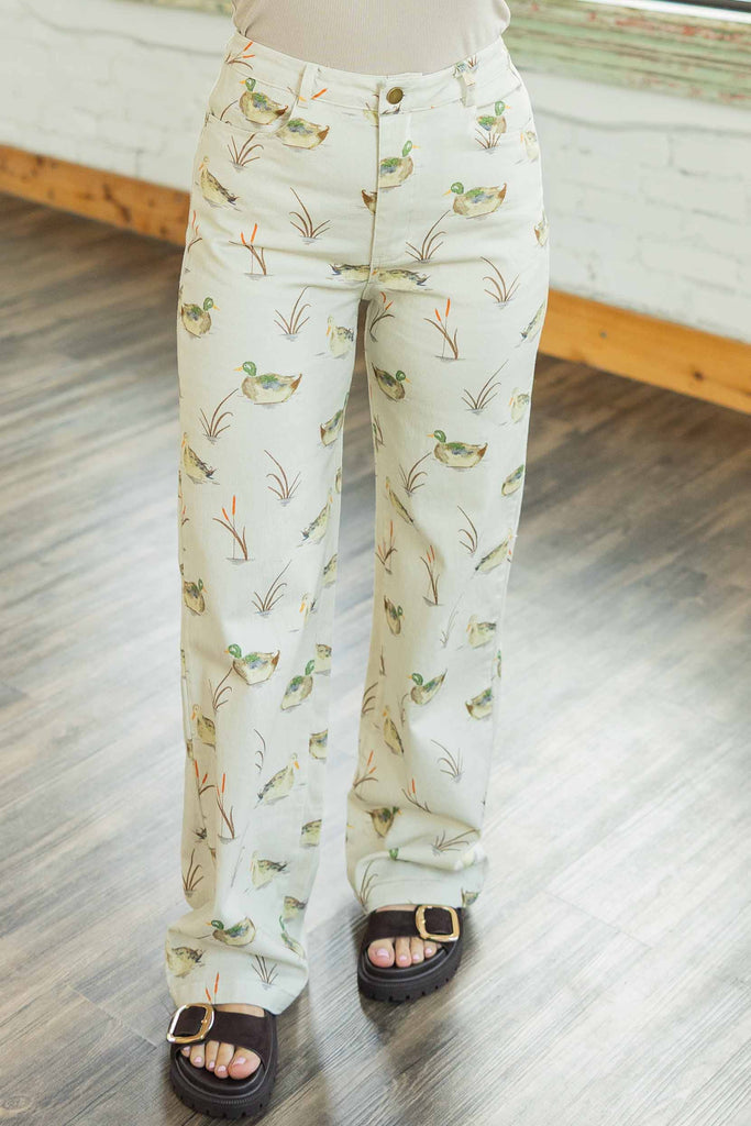 Woman wearing cream high rise straight leg jeans with allover mallard duck print paired with a brown top in a bright loft space.