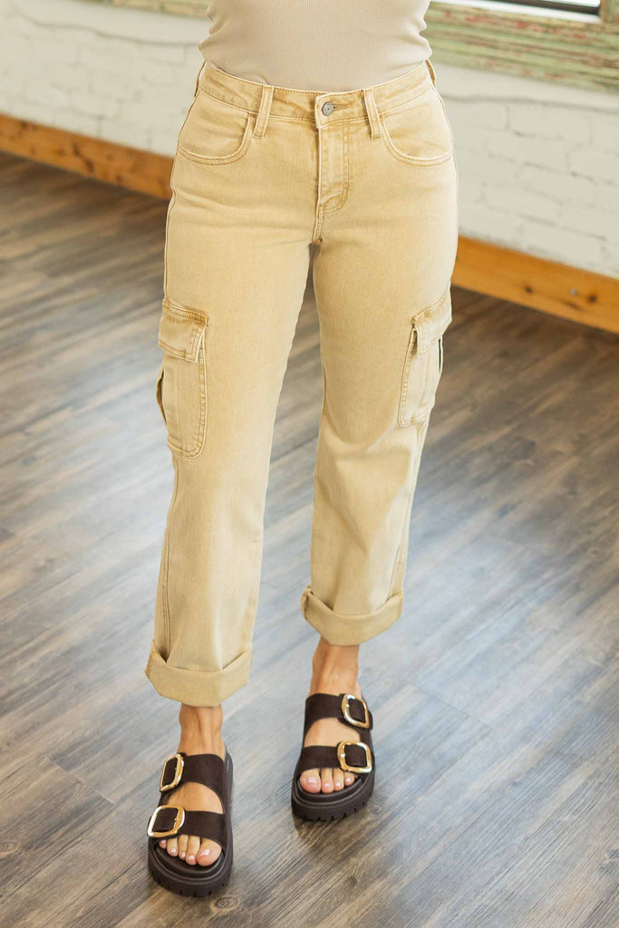 Woman wearing high rise sand-colored relaxed straight cargo jeans with multiple pockets and cuffed hems in a bright loft space.