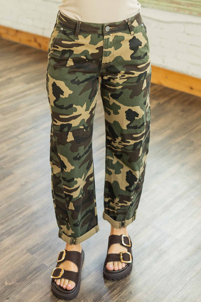 Woman wearing high rise camo barrel-leg jeans with double rolled ankle cuffs paired with a brown graphic tee in a bright loft space.
