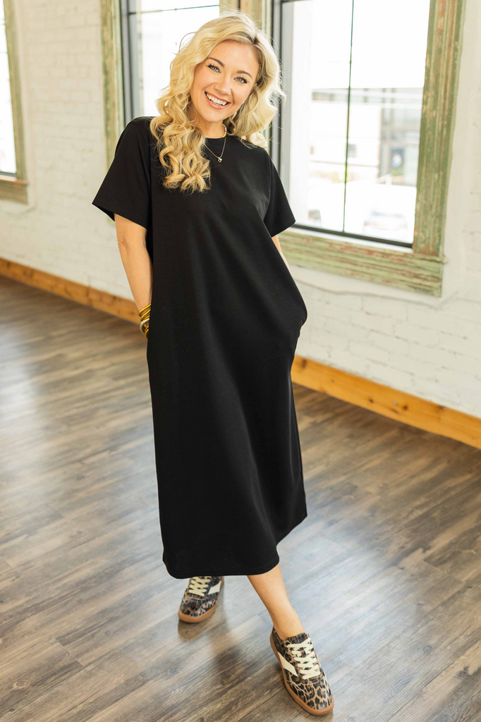 Woman wearing a black ribbed midi pullover dress with short sleeves and side pockets styled with leopard sneakers in a bright loft.