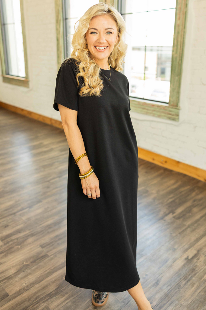 Woman wearing a black ribbed midi pullover dress with short sleeves and side pockets styled with leopard sneakers in a bright loft.