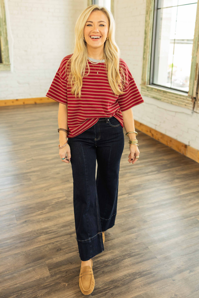 Woman wearing a relaxed red striped cropped tee with ivory contrast neckline, styled with dark denim jeans in a bright indoor space.