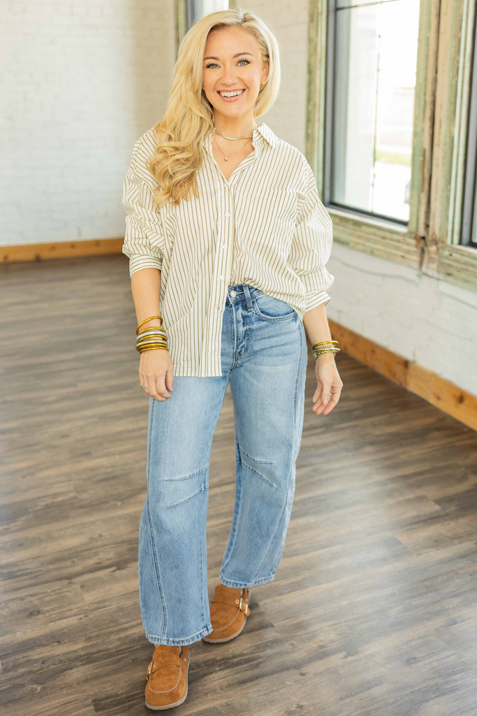 Woman wearing oversized grey and taupe striped button-up boyfriend shirt styled with light wash denim BARREL jeans.
