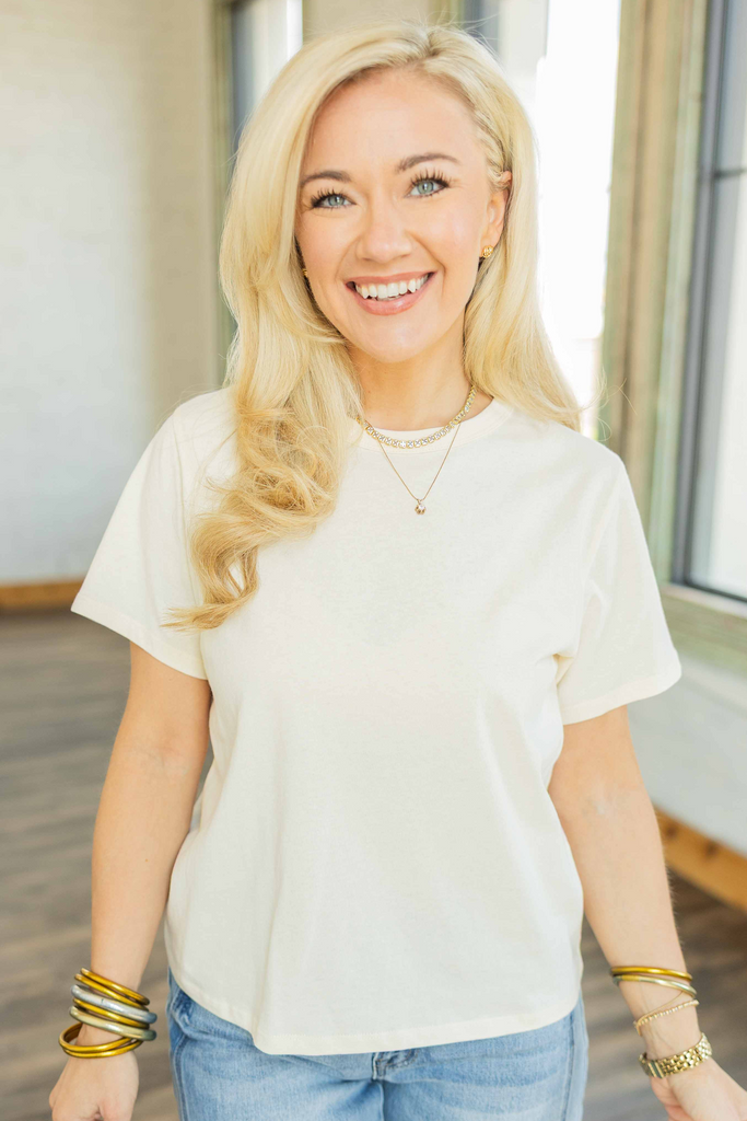Woman wearing vanilla short sleeve relaxed boxy cotton top styled with light wash denim jeans.