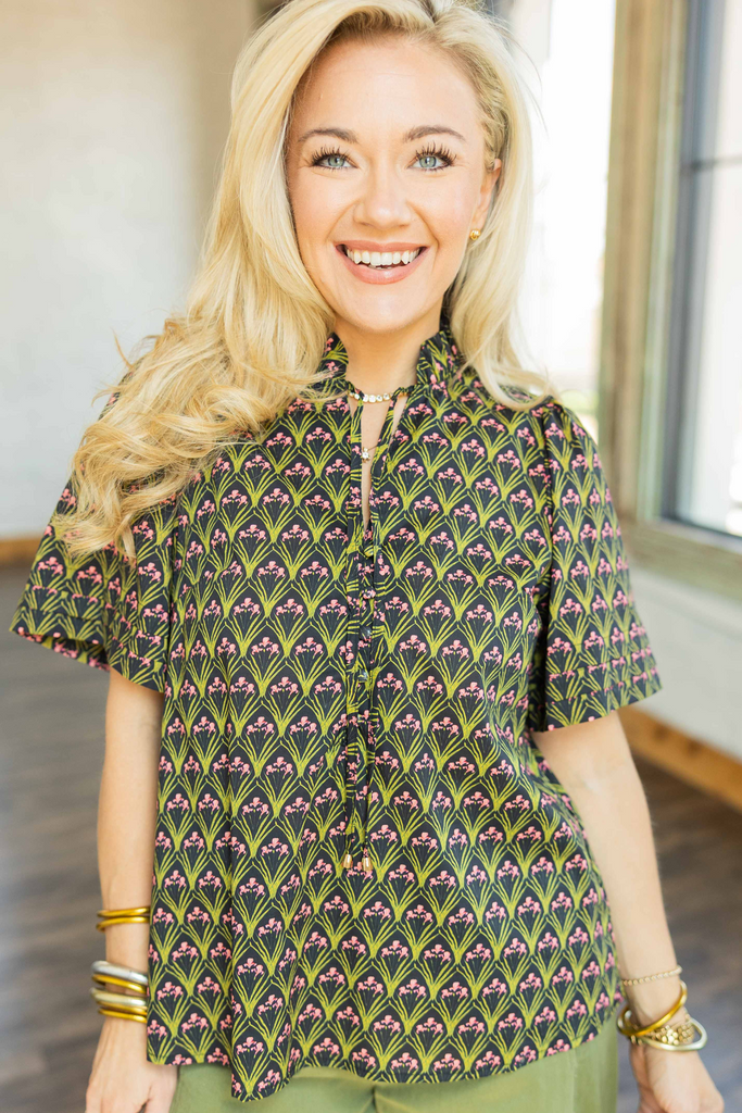 Woman wearing black top with green and pink geometric print, ruffled mock neck, and short sleeves styled with olive wide-leg pants.