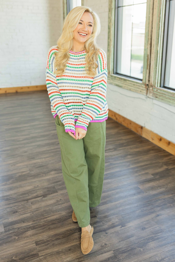 Woman wearing a colorful striped sweater and green pants indoors.