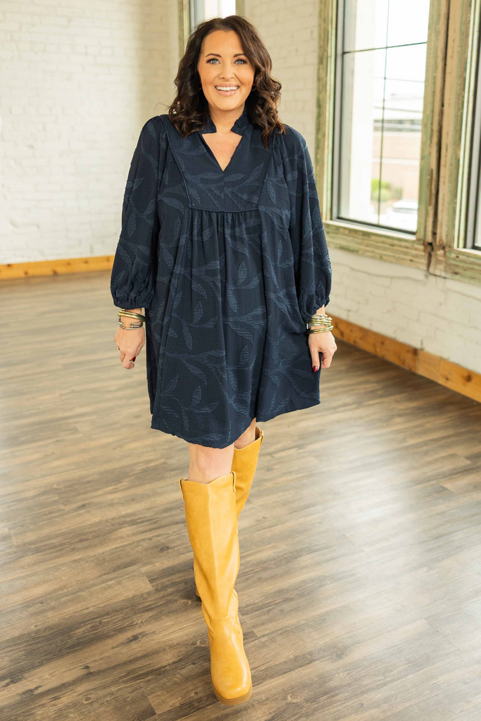  plus Woman wearing a navy mini dress with tonal leaf jacquard texture, ruffle collar, and long puff sleeves and yellow boots