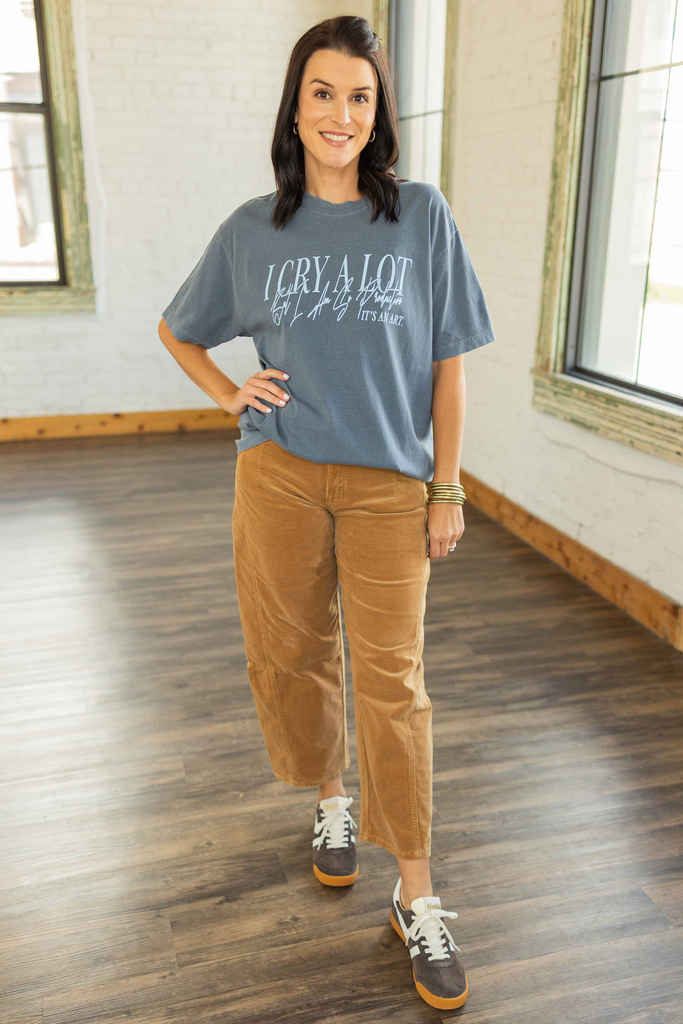 wearing a blue oversized graphic tee that says “I Cry A Lot, It’s An Art” paired with camel corduroy pants and sneakers.