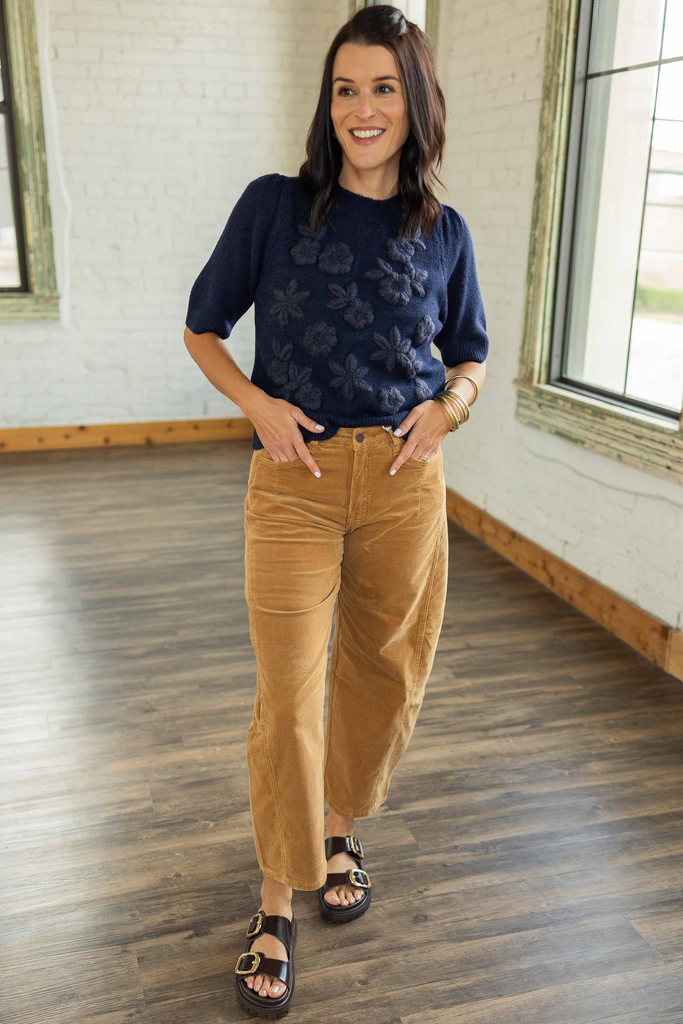 Kandace wearing caramel corduroy barrel jeans with a navy short sleeve sweater and dark buckle sandals.