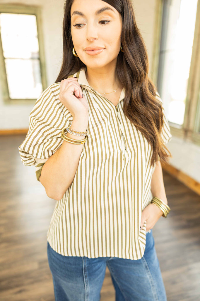 Kayla wearing a cream and olive green striped quarter zip pullover top with contrast collar and elastic hem, paired with denim jeans.