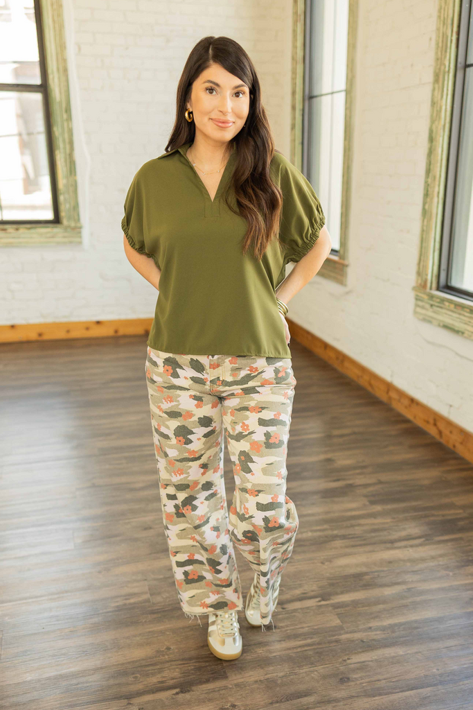 Kayla wearing an olive green short sleeve top with split collar and side slits, paired with floral camo wide-leg pants.