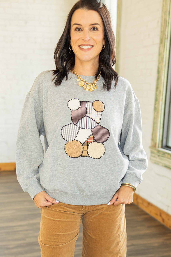 Kandace wearing a gray crewneck pullover with a multi-texture patchwork teddy bear design on front, paired with camel corduroy pants