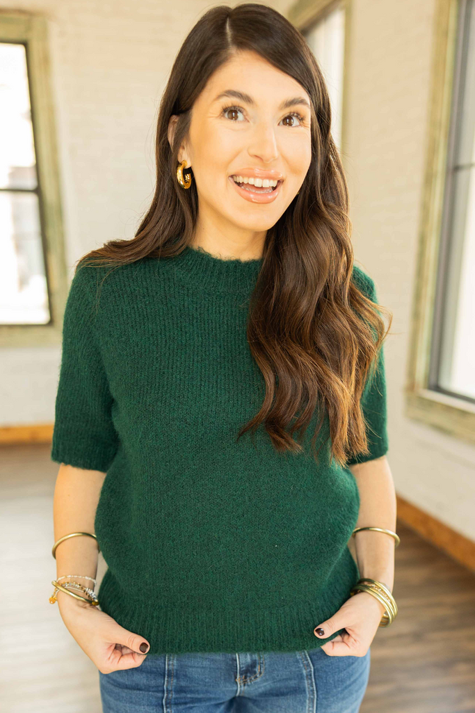 Kayla wearing a forest green short sleeve sweater knit top with a crew neckline, paired with medium wash denim jeans.