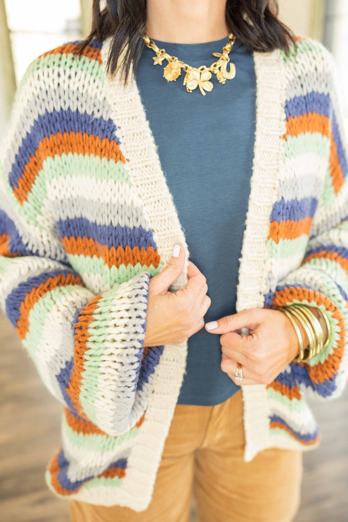Kandace wearing an oversized striped knit cardigan in rust, navy, olive, and cream tones over a blue top with camel corduroy pants