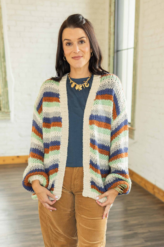 Kandace wearing an oversized striped knit cardigan in rust, navy, olive, and cream tones over a blue top with camel corduroy pants