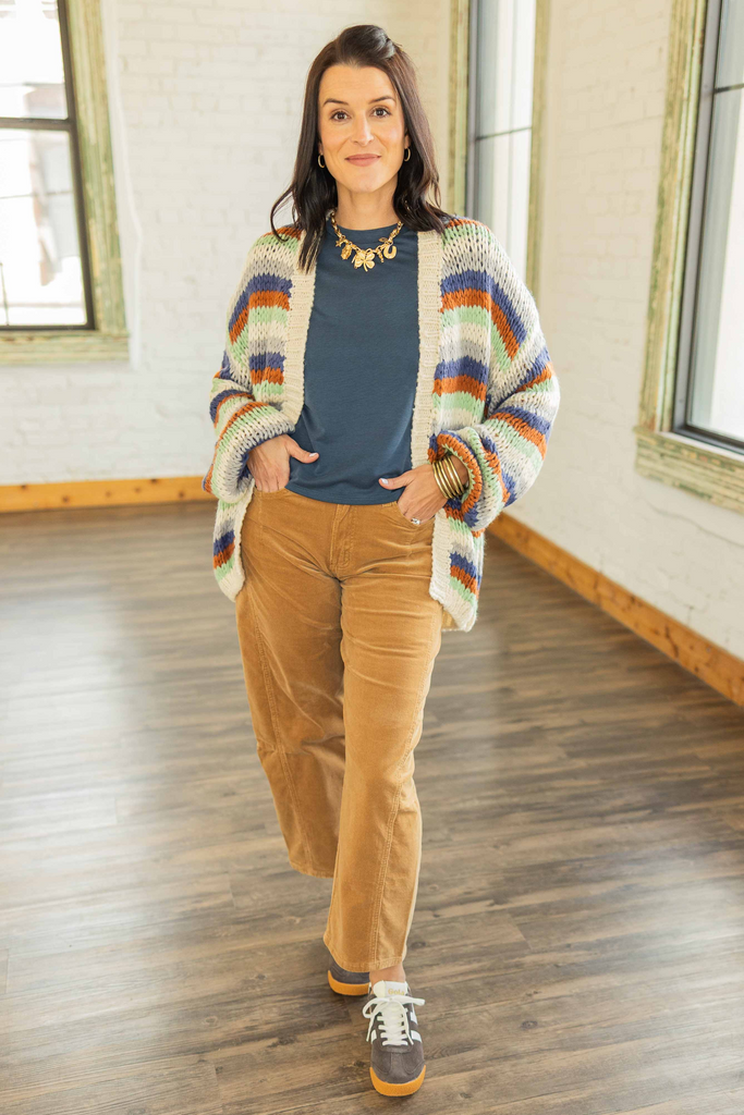 Kandace wearing an oversized striped knit cardigan in rust, navy, olive, and cream tones over a blue top with camel corduroy pants