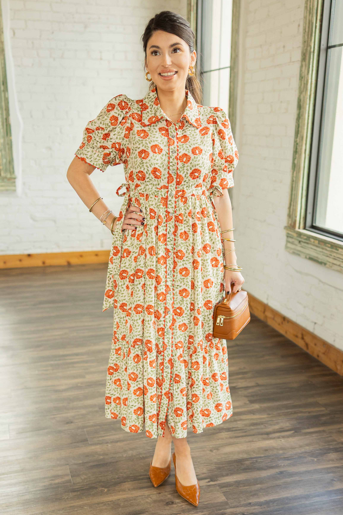  Kayla wearing cream midi dress with burnt orange floral print, puff sleeves with scalloped cuffs, tie waist, and button-front design.