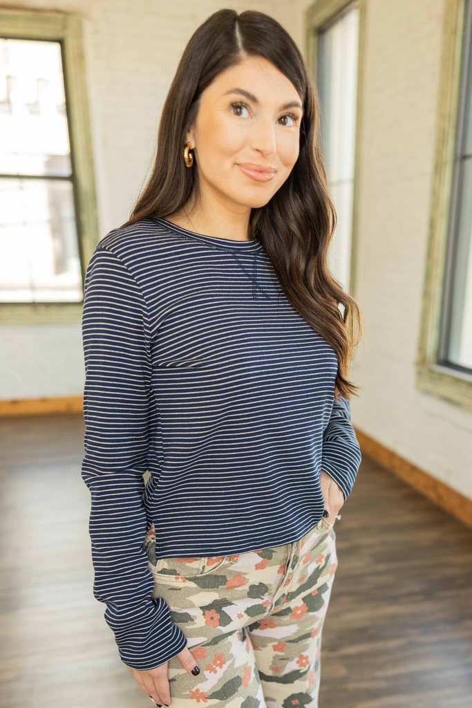 Kayla wearing a navy and ivory striped long sleeve knit top with side slits, paired with floral camo wide-leg pants.