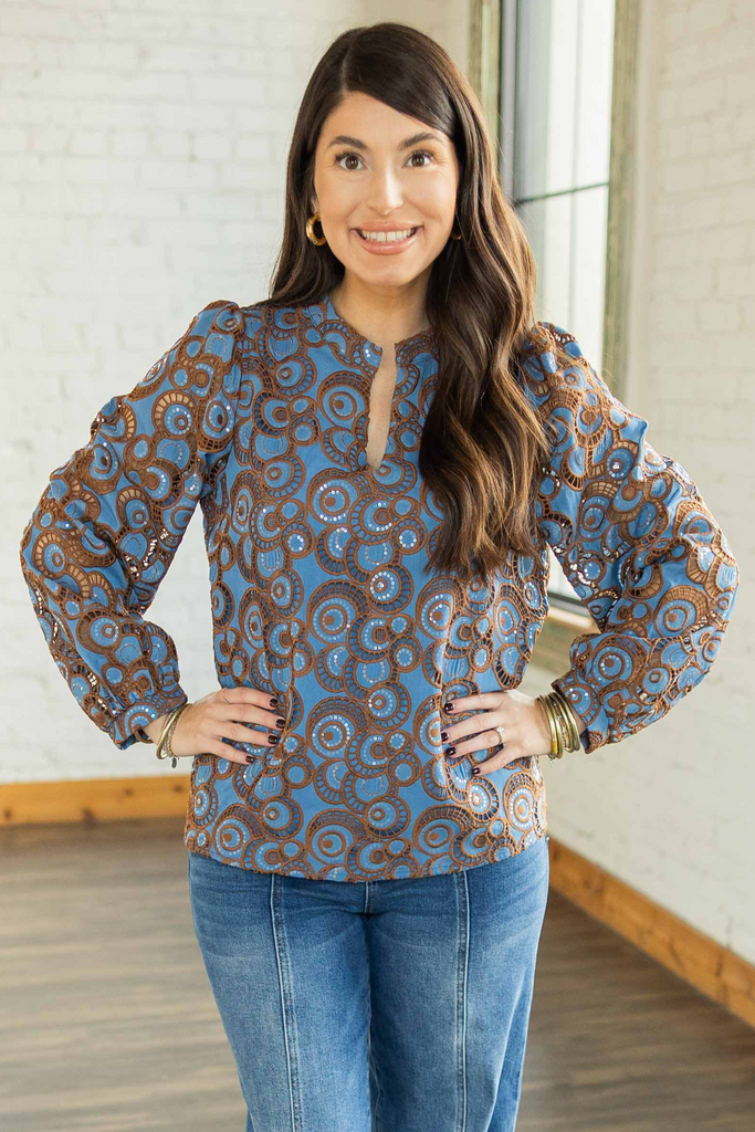 Kayla wearing a blue long sleeve top with copper embroidered and sequin circular pattern, sheer sleeves, and lined bodice, paired with denim jeans.