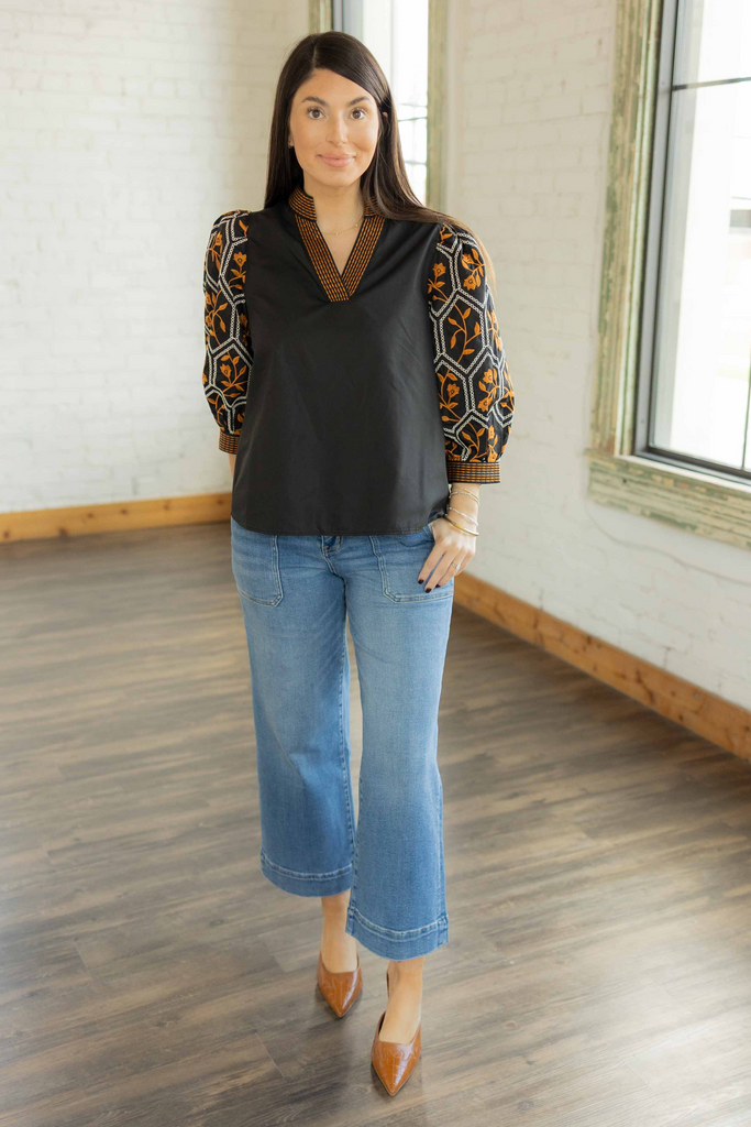Kayla wearing the Leia black pullover top with orange and cream embroidered 3/4 sleeves and neckline paired with light wash jeans