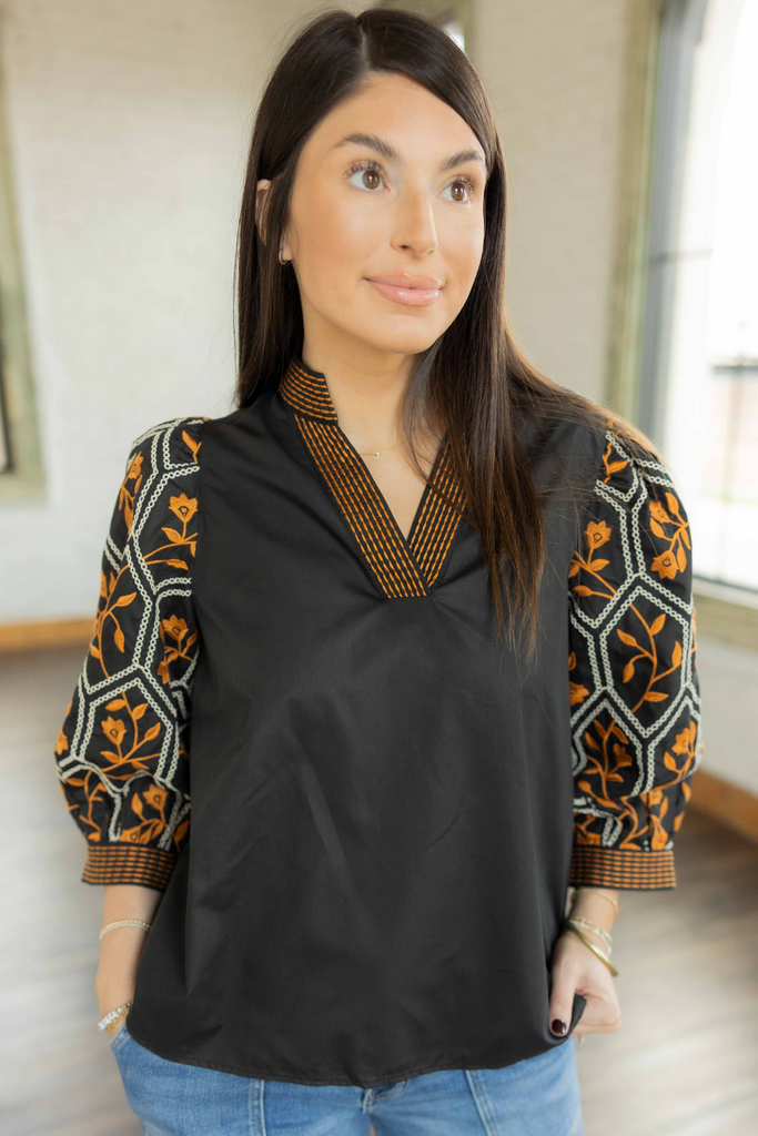 Kayla wearing the Leia black pullover top with orange and cream embroidered 3/4 sleeves and neckline paired with light wash jeans