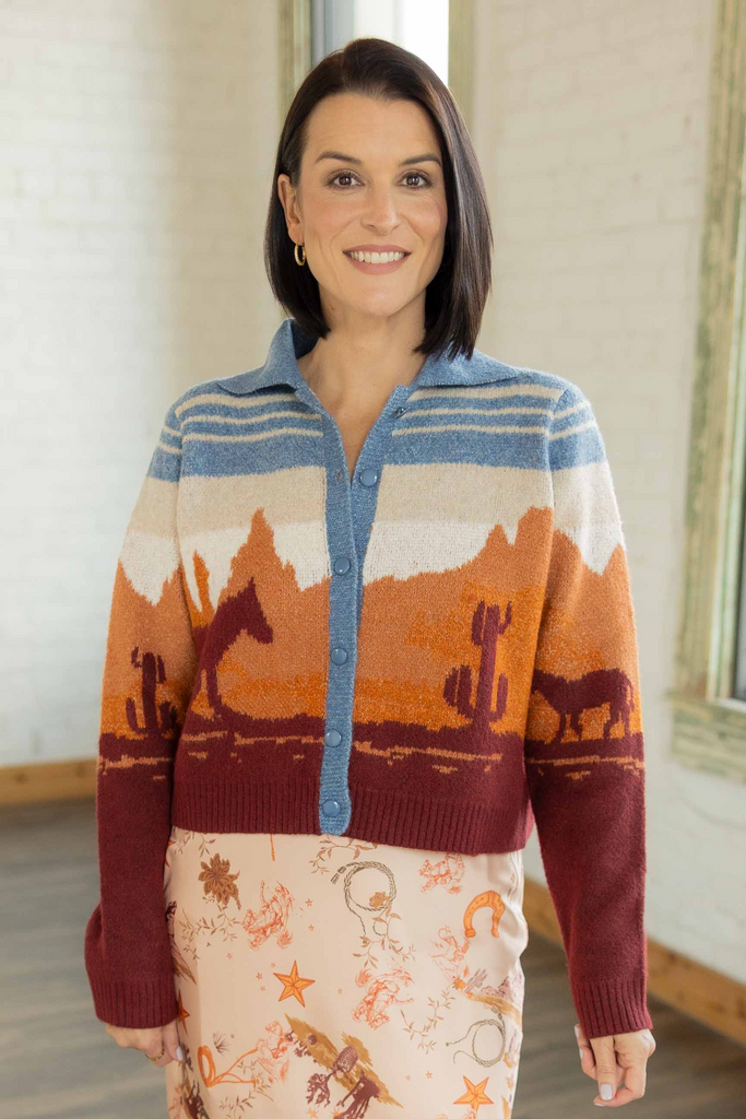 Kandace wearing the Brooke western print cardigan in rust, blue, and ivory tones with desert landscape design, paired with a printed midi skirt