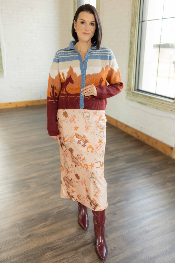 Kandace wearing the Brooke western print cardigan in rust, blue, and ivory tones with desert landscape design, paired with a printed midi skirt