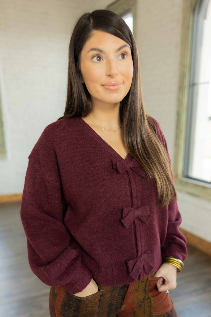 Kayla wearing the Ava burgundy knit pullover sweater with bow details down the front, paired with printed patchwork pants